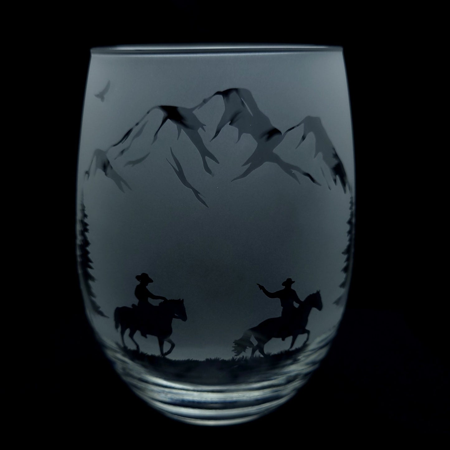 etched western themed cocktail glass of cowboys on horseback riding through the forest and mountains, 