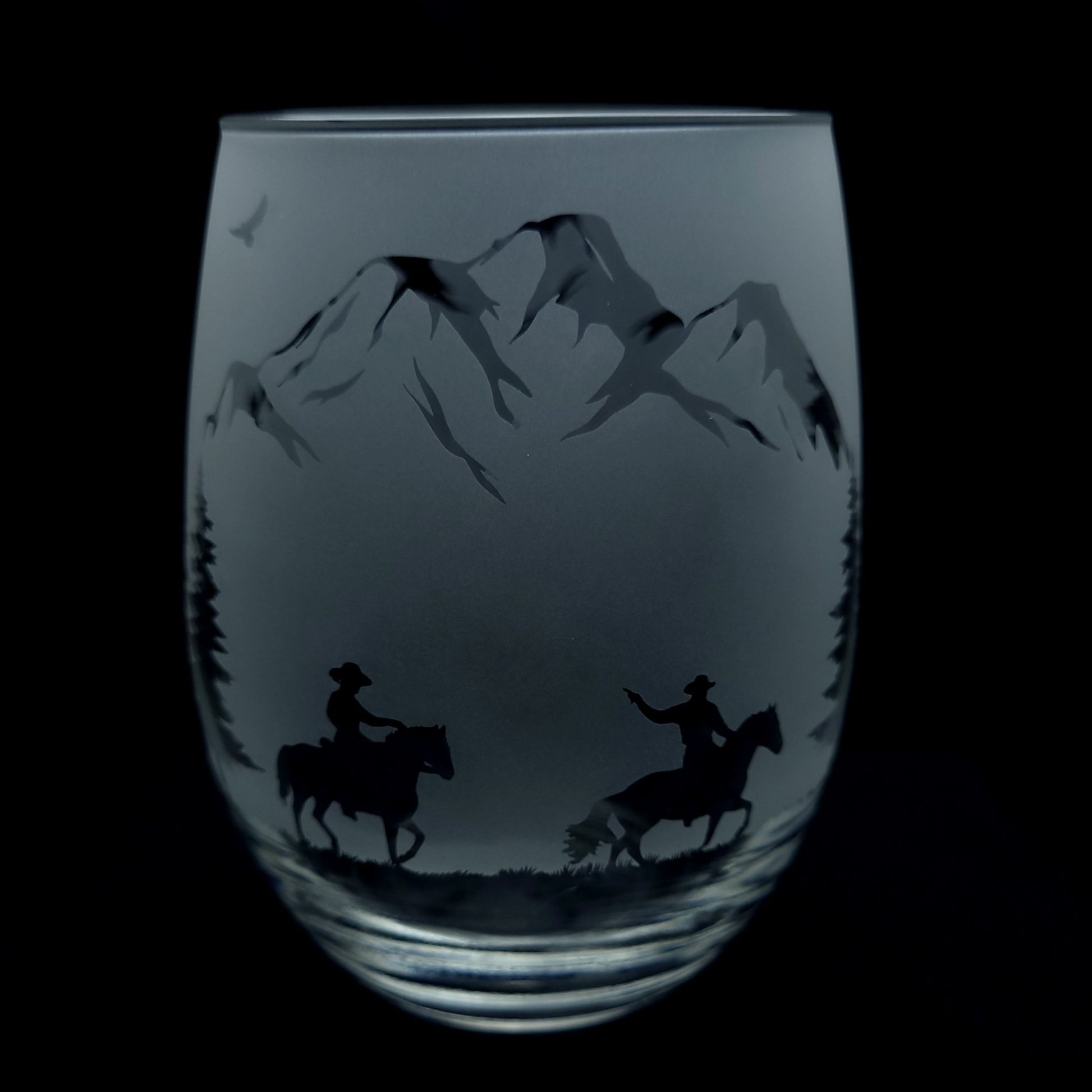 etched western themed cocktail glass of cowboys on horseback riding through the forest and mountains, 