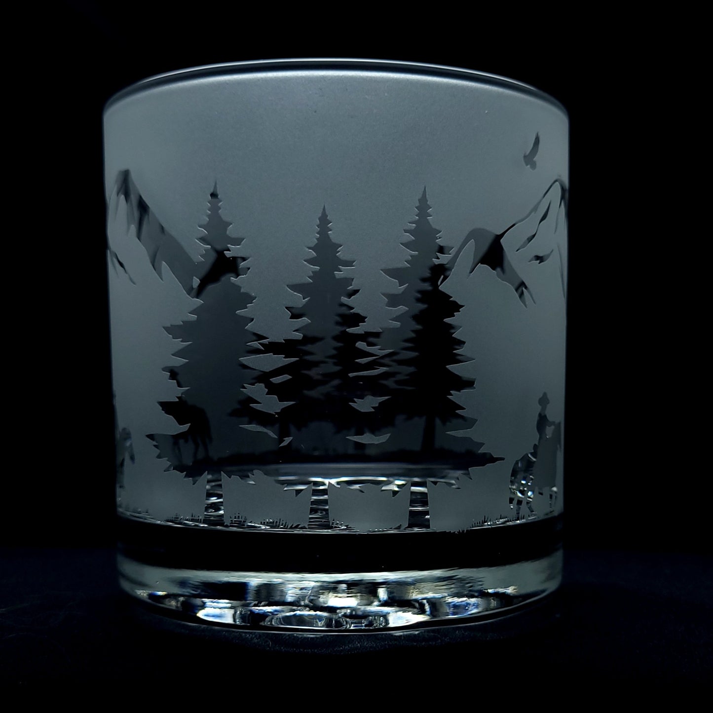 etched nature forest trees on a background of a western themed cocktail glass with cowboys on horseback riding through the mountains.
