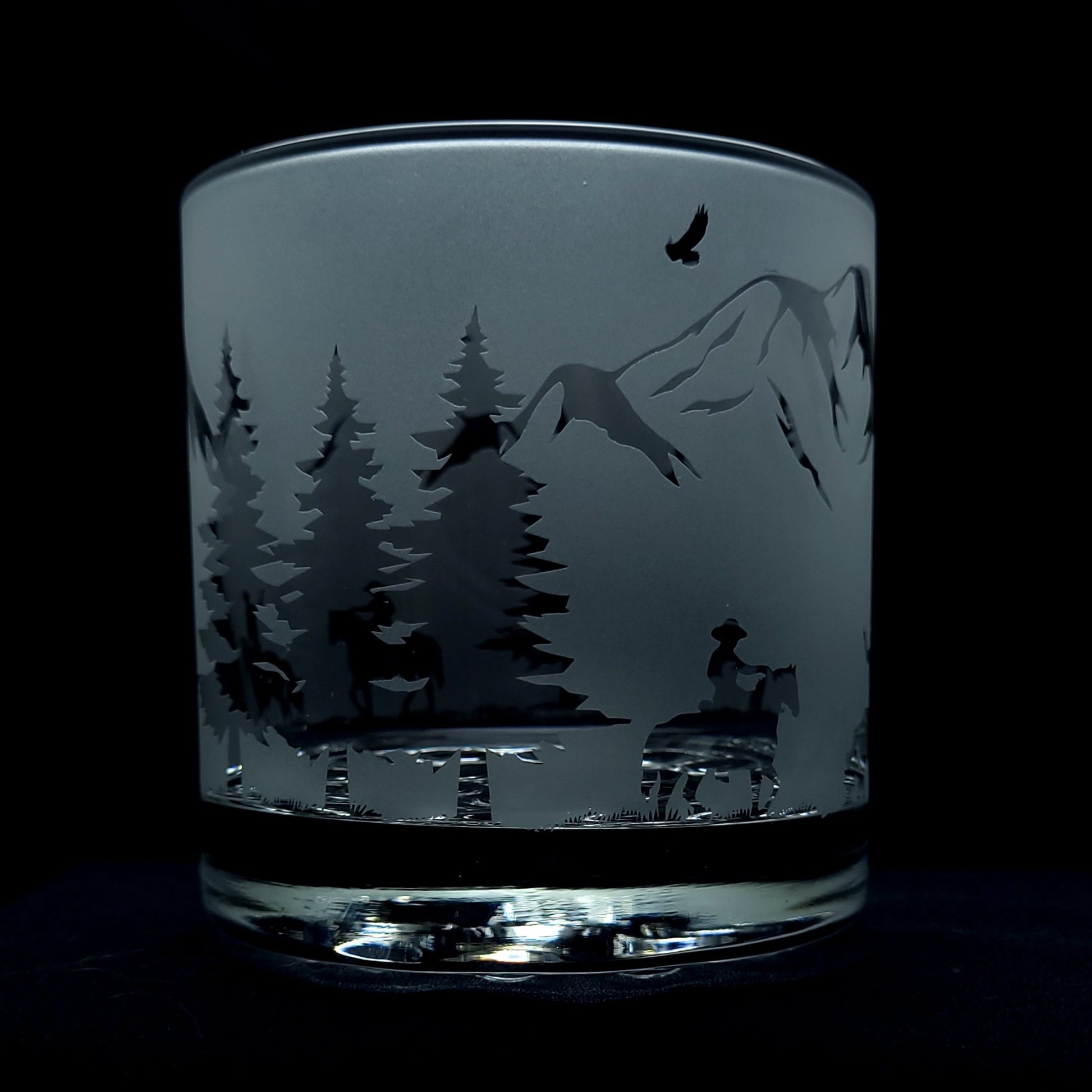 etched western themed cocktail glass which features cowboys on horseback riding through the mountains guns drawn, an eagle flying above in the clear sky
